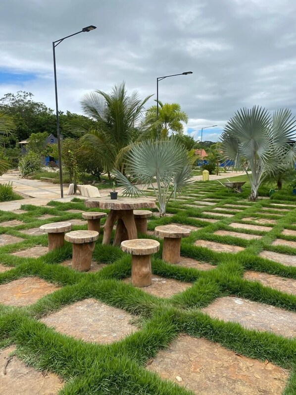 Un jardin avec des tables et des chaises en pierre, entouré de pelouse et de palmiers.