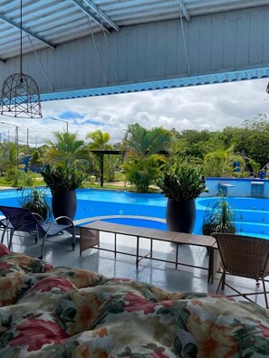 Zona junto a la piscina con sillones de descanso y plantas en macetas, una piscina azul cristalina y vistas de la vegetación circundante.