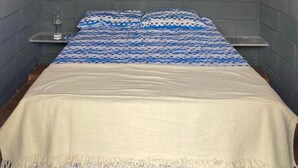 A bedroom with a sloped ceiling, a bed with patterned bedding, a bedside table, and an air conditioning unit. - Pousada Ramilos - Sertão (Tiangua)