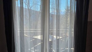 Una ventana con cortinas blancas traslúcidas, vistas a mesas exteriores y un cielo azul despejado.