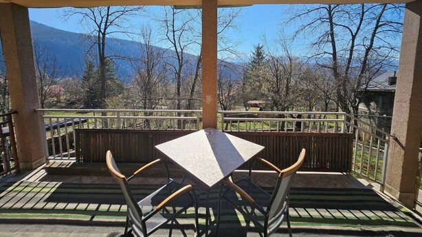 Un patio cubierto con una mesa y sillas, vistas a montañas y una cerca de madera.