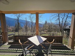 A covered patio with a table and chairs, a view of mountains, and a wooden fence.