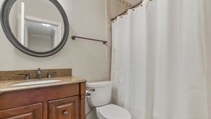 Une salle de bain avec un meuble-lavabo en bois, un miroir rond, des toilettes et un rideau de douche.