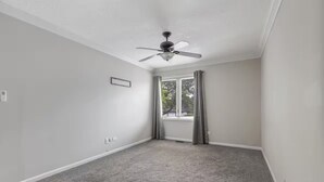 Une pièce dotée d’un ventilateur de plafond, d’une fenêtre avec des rideaux et d’un plancher recouvert de moquette.