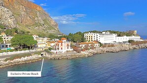 A coastal town with buildings, a rocky shoreline, and a clear blue sky. - Mondello D'Amare (Palermo)