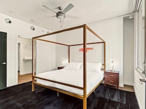 A modern bedroom with a four-poster bed, a ceiling fan, and a bedside table with a lamp.