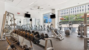 Un gimnasio con diversos equipos de ejercicio, ventanas amplias y un ventilador de techo.