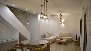 Uma sala de estar moderna com uma mesa de jantar de vidro, cadeiras de madeira, um sofá bege e uma escada com parede de pedra.