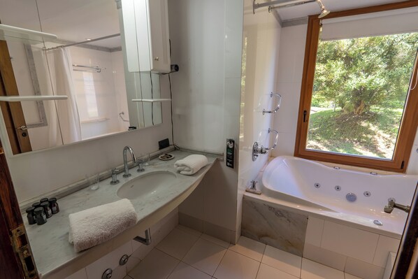 A modern bathroom with a large bathtub, a vanity with a mirror, and a window providing a view of greenery. - Rent Up -Casa junto al lago Nahuel Huapi (Villa La Angostura)