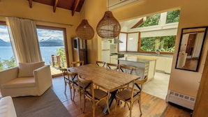 Un amplio espacio habitable con una mesa de comedor de madera, asientos cómodos y un ventanal con vistas a un lago y montañas.
