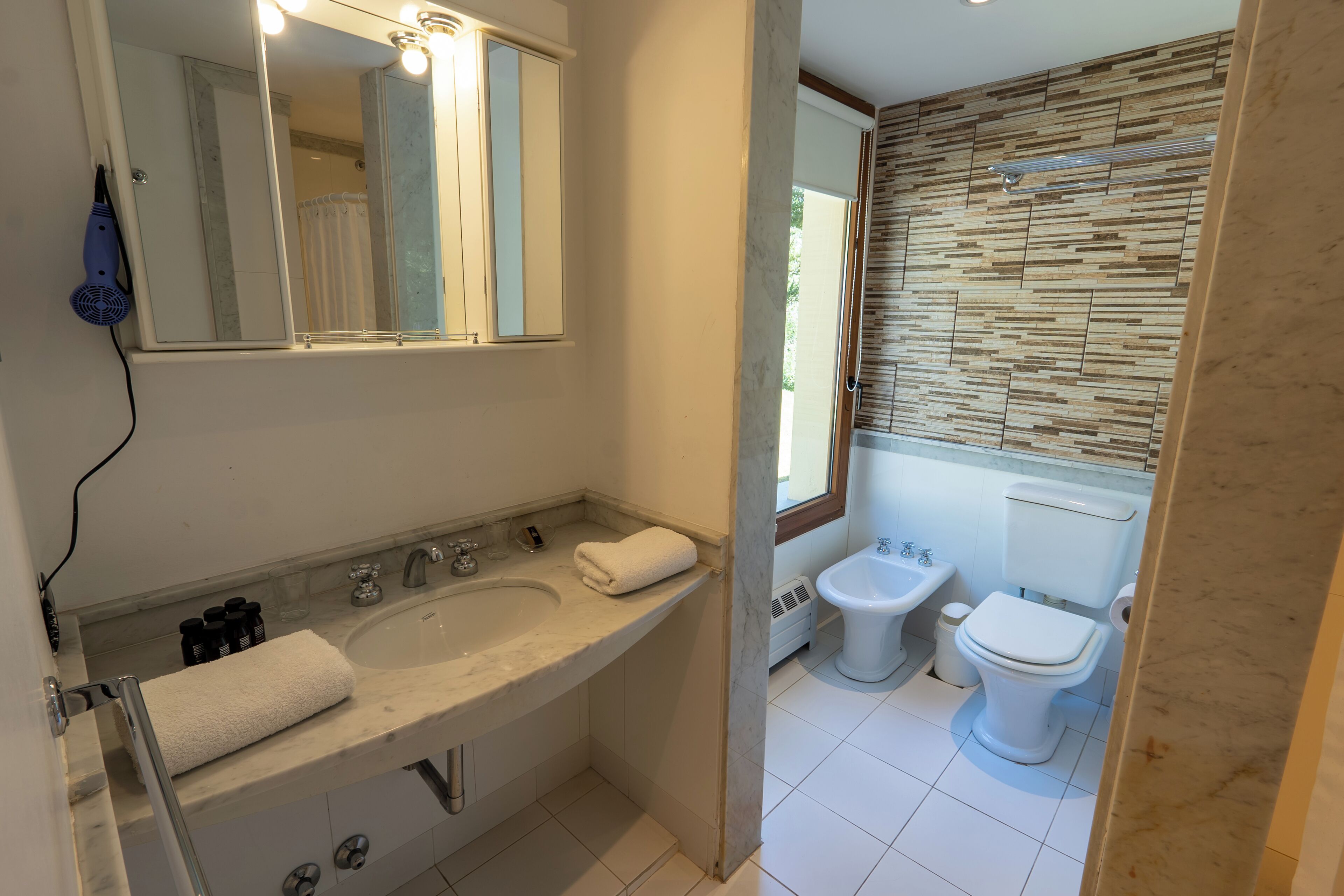 A bathroom with a double sink, a mirror, a towel, a bidet, and a toilet.