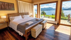 Un dormitorio con una cama grande, un banco y vistas a un lago y montañas.