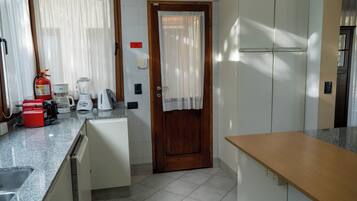 Una cocina compacta con puerta de madera, armarios blancos, una encimera con cafetera, licuadora y un tostador rojo.