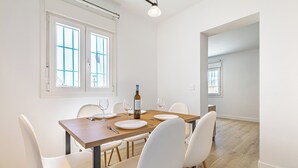Un coin repas avec une table en bois, des chaises blanches et une bouteille de vin.
