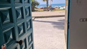 Une porte qui donne sur une vue de la plage, avec un palmier et un ciel dégagé.