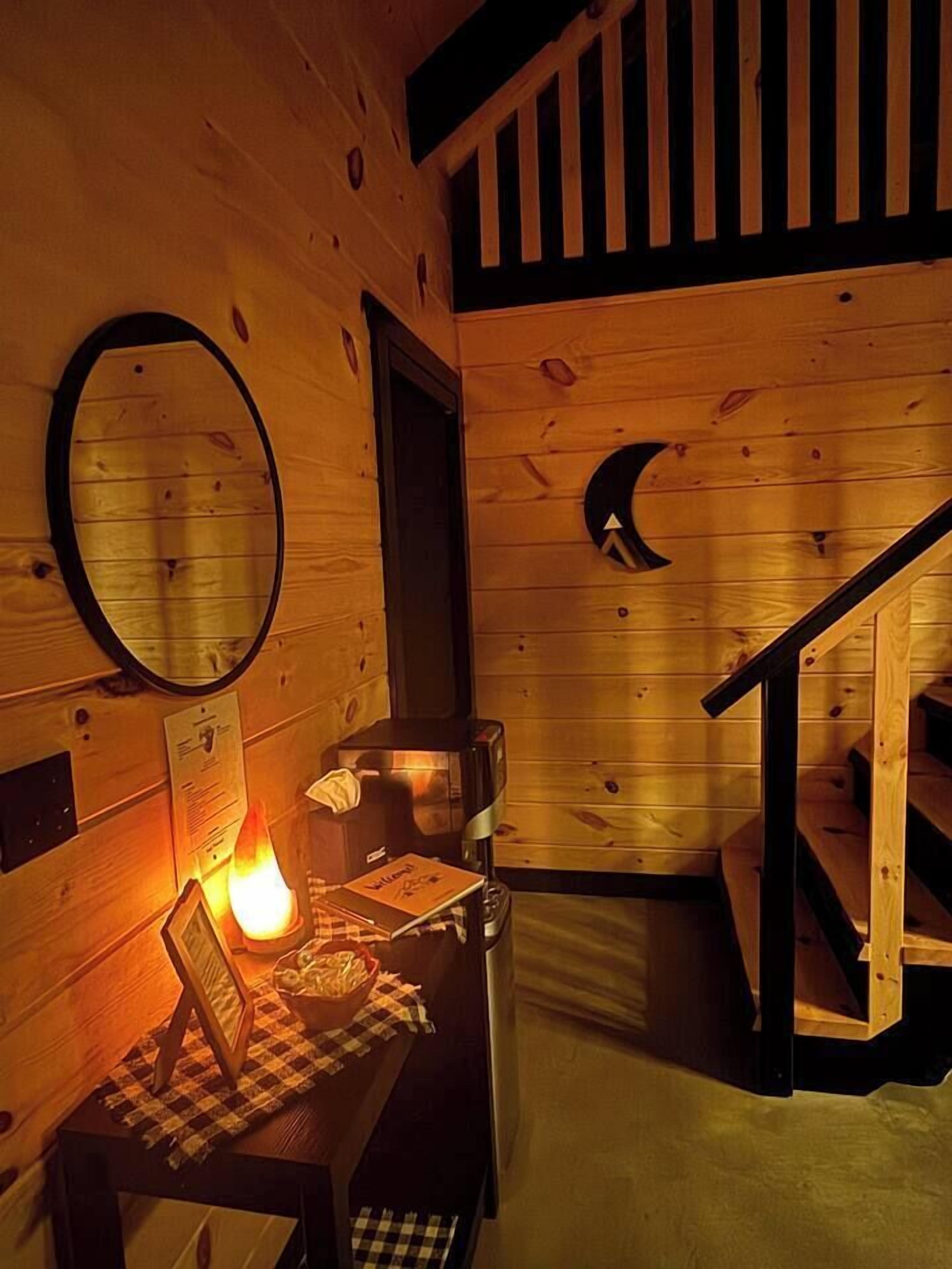 A wooden cabin interior with a fireplace, a mirror, a wooden staircase, and a checkered tablecloth.
