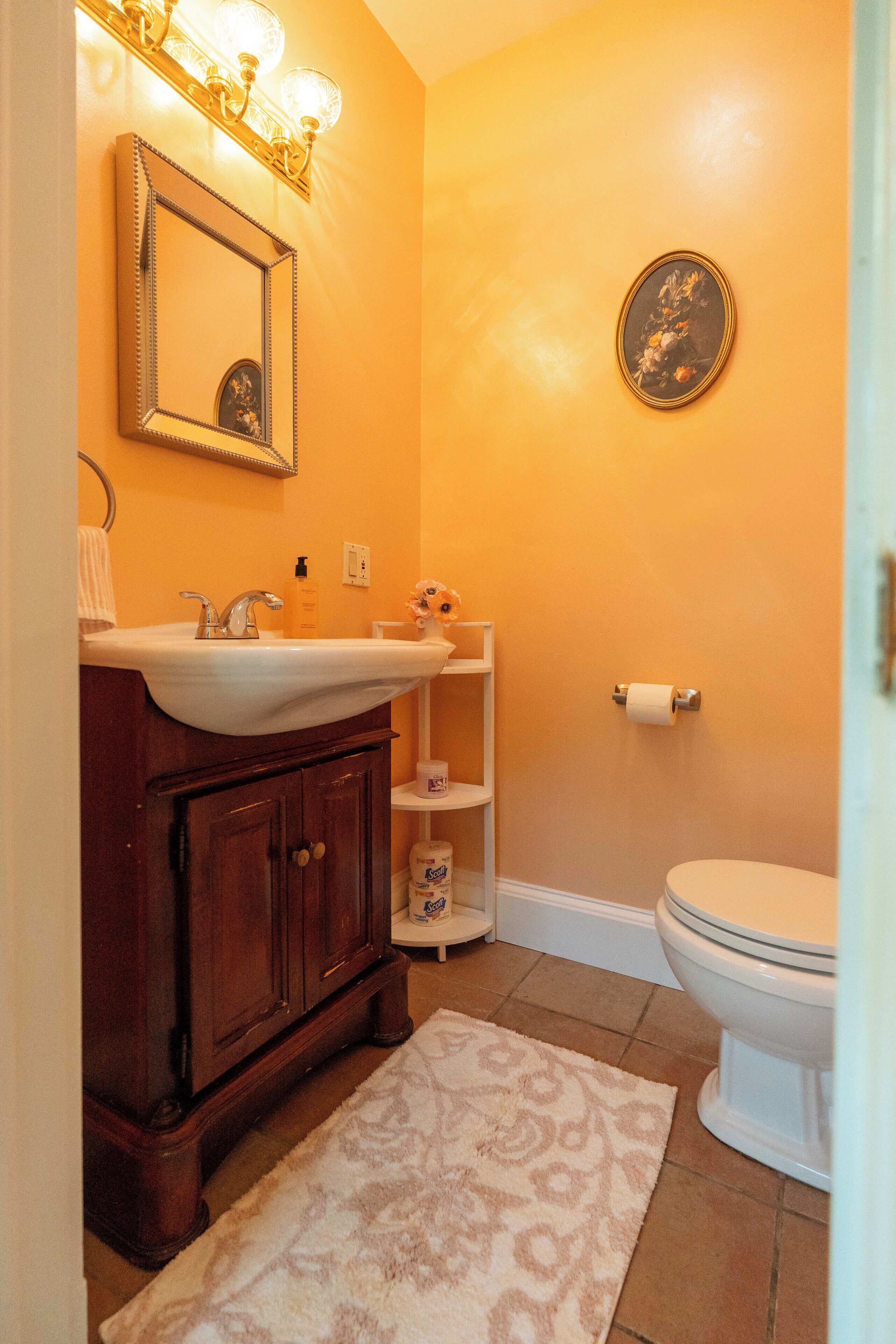 A bathroom with a wooden vanity, a white sink, a mirror, a toilet, and a patterned rug.