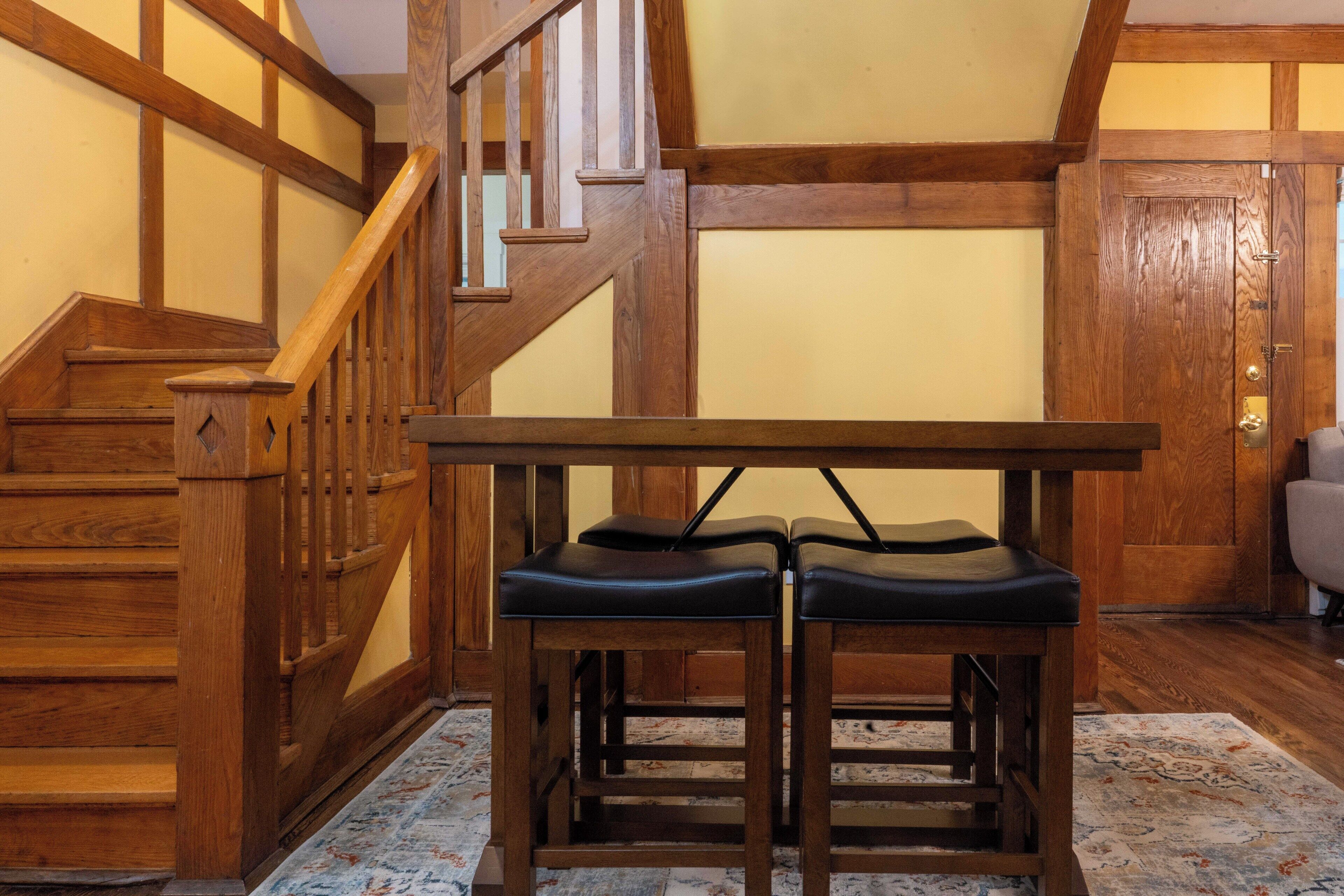 A wooden staircase with a handrail, a wooden table with two chairs, and a patterned rug on the floor.