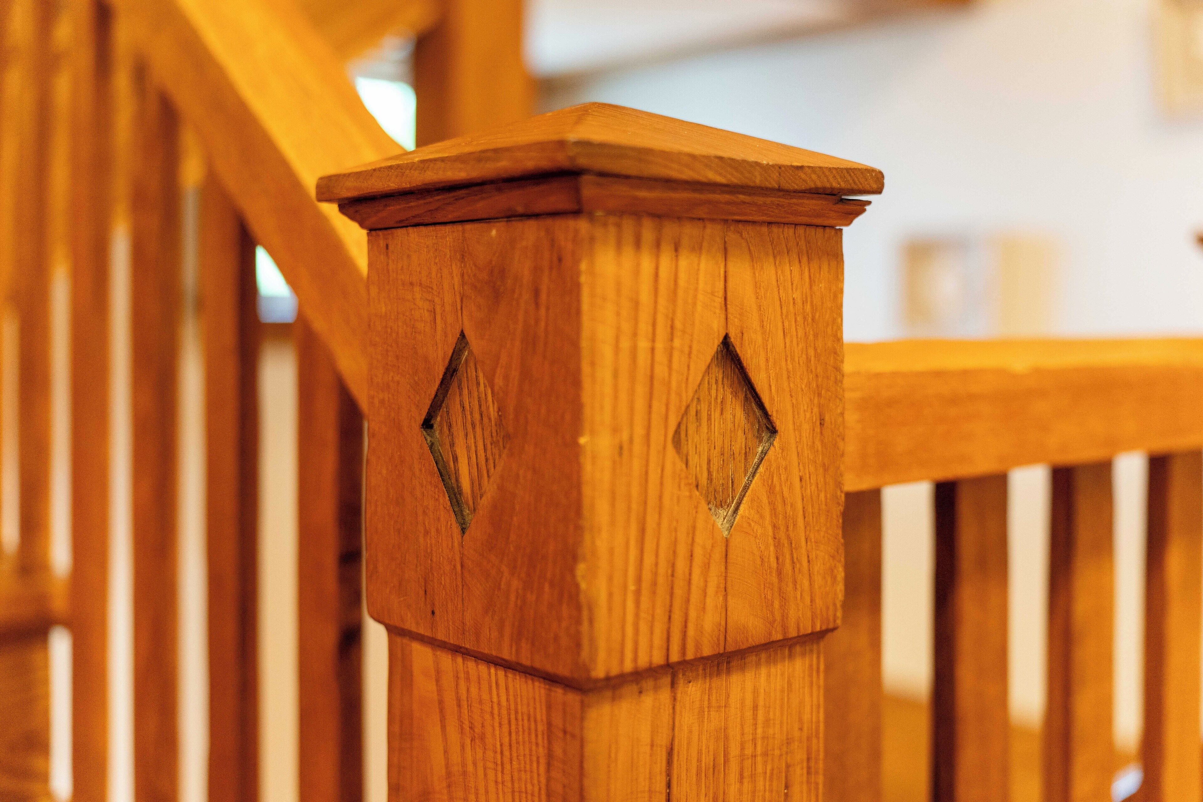 Een houten trap met een leuning en een houten paal met diamantvormige uitsparingen.