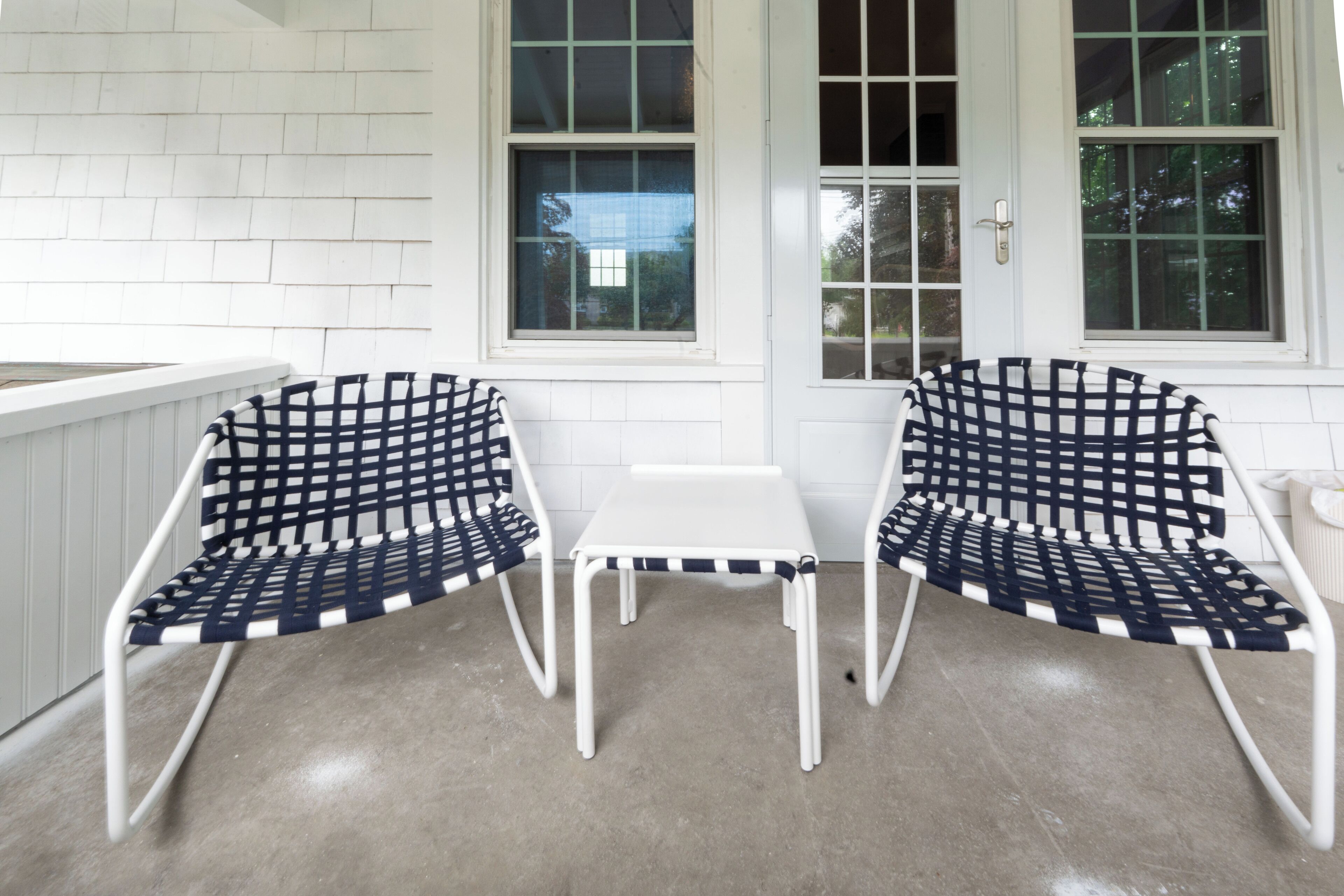 A patio with two metal chairs and a small table, white walls, and large windows.