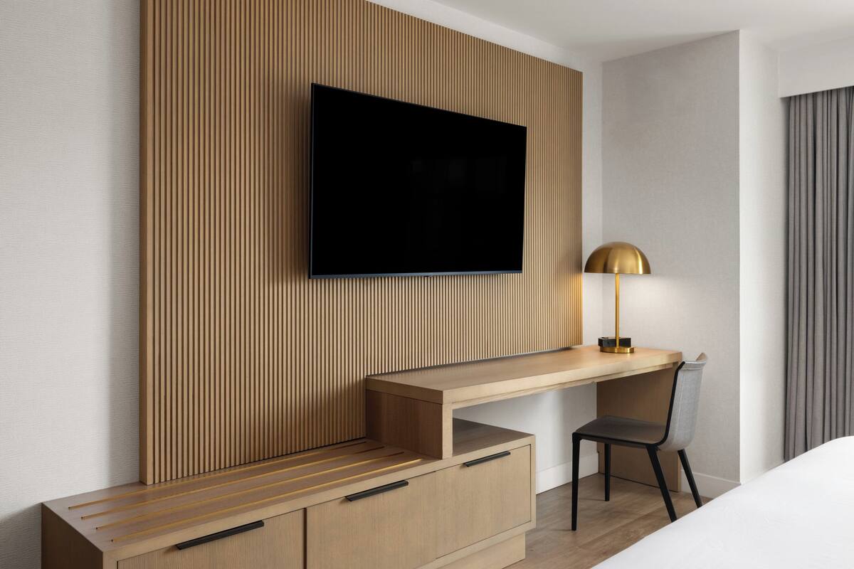 A modern room with a flat-screen TV mounted on a wooden panel wall, a desk with a chair, and a lamp.