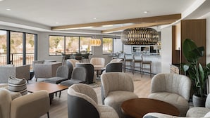 Un moderno vestíbulo de hotel con zonas de estar, un bar y ventanas grandes.