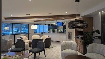 A modern hotel lobby with seating areas, a bar, and large windows offering city views.