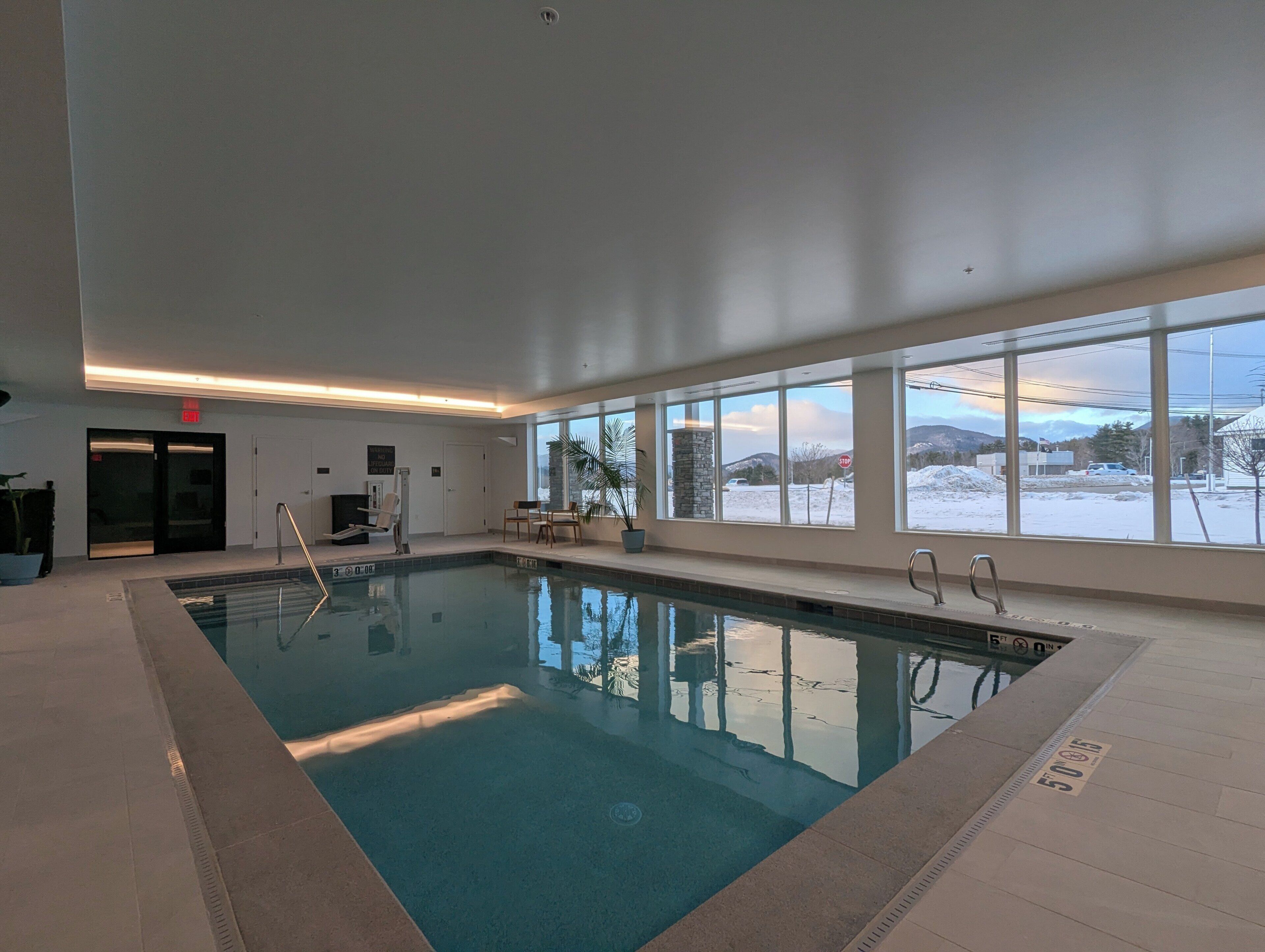 Una piscina interior con paredes de vidrio transparente, una silla de salvavidas y vistas a un paisaje nevado a través de grandes ventanales.