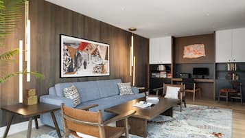 A modern living room with a sofa, coffee table, chairs, a TV, and a kitchen area.
