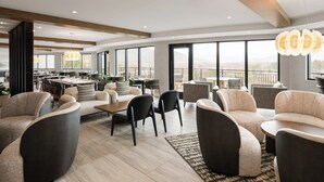 Amplia sala de estar con muebles modernos, ventanas grandes que ofrecen vistas a las montañas y un bar al fondo.