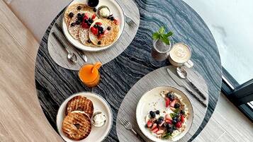 A breakfast setting with pancakes, bagels, and fruit on plates, a glass of orange juice, and a cup of coffee on a round table.