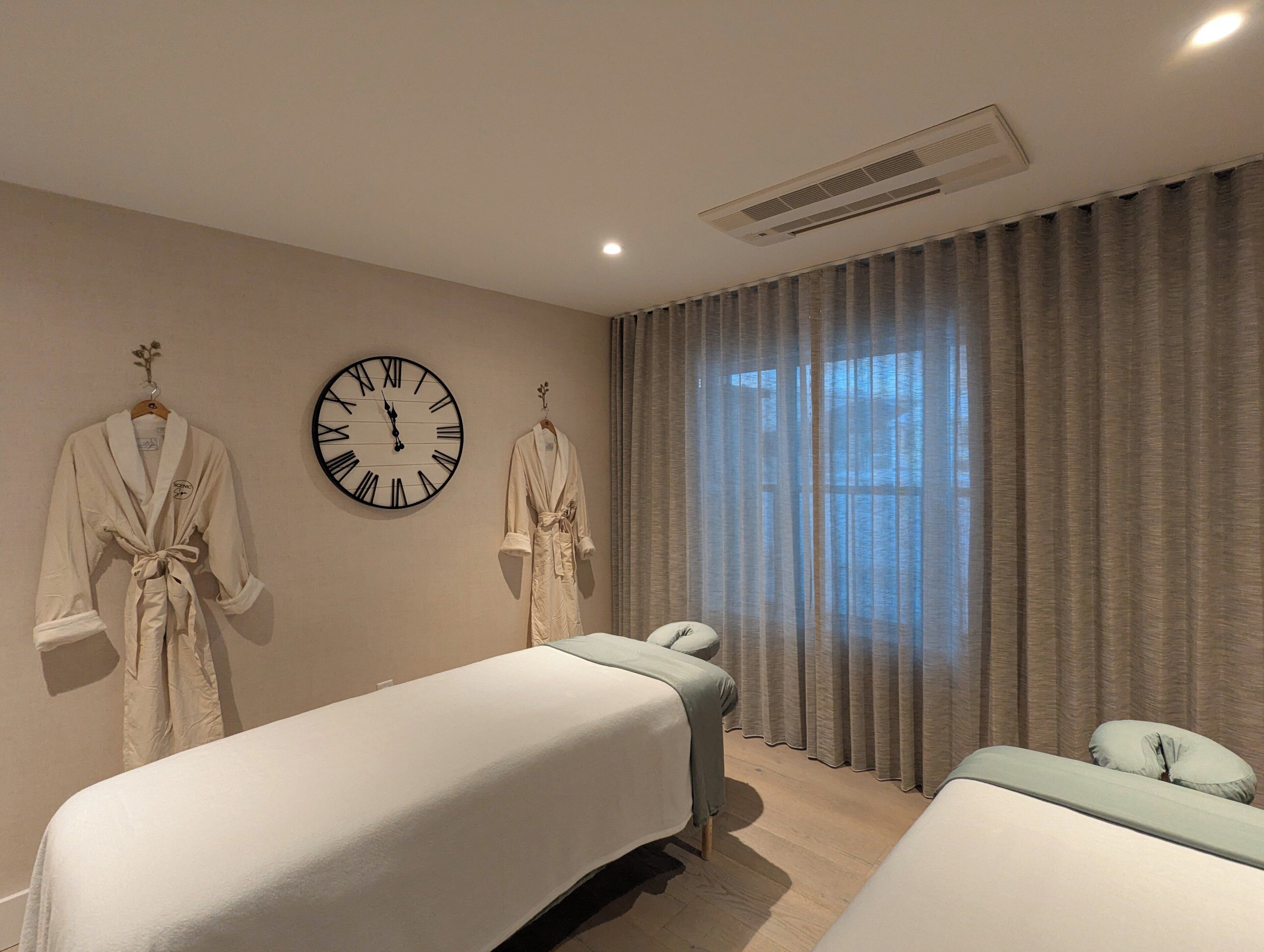 A hotel room with two beds, a large wall clock, and a window with curtains.