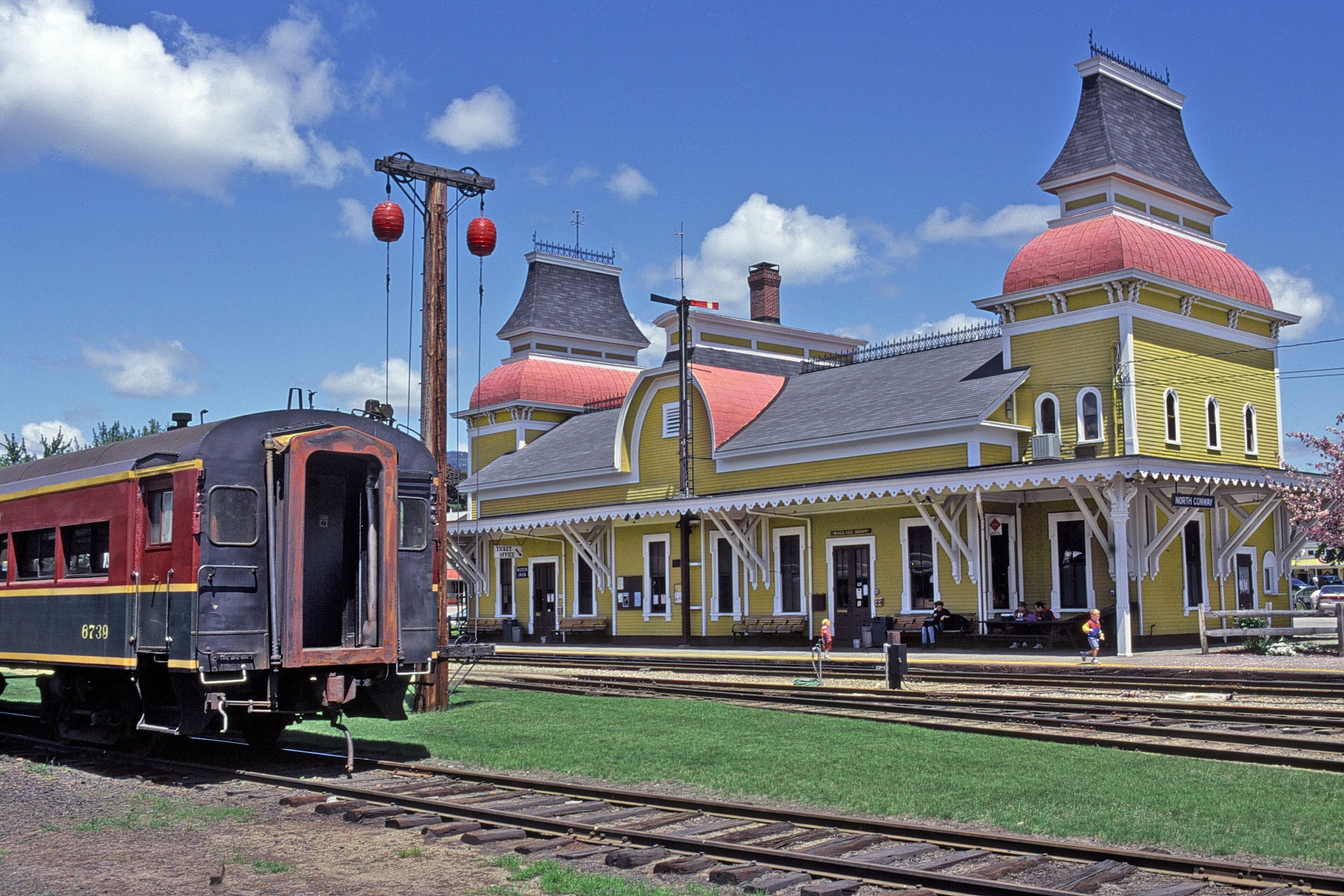 Ein gelber Bahnhof mit roter Kuppel und einem schwarzen Zug auf den Gleisen.