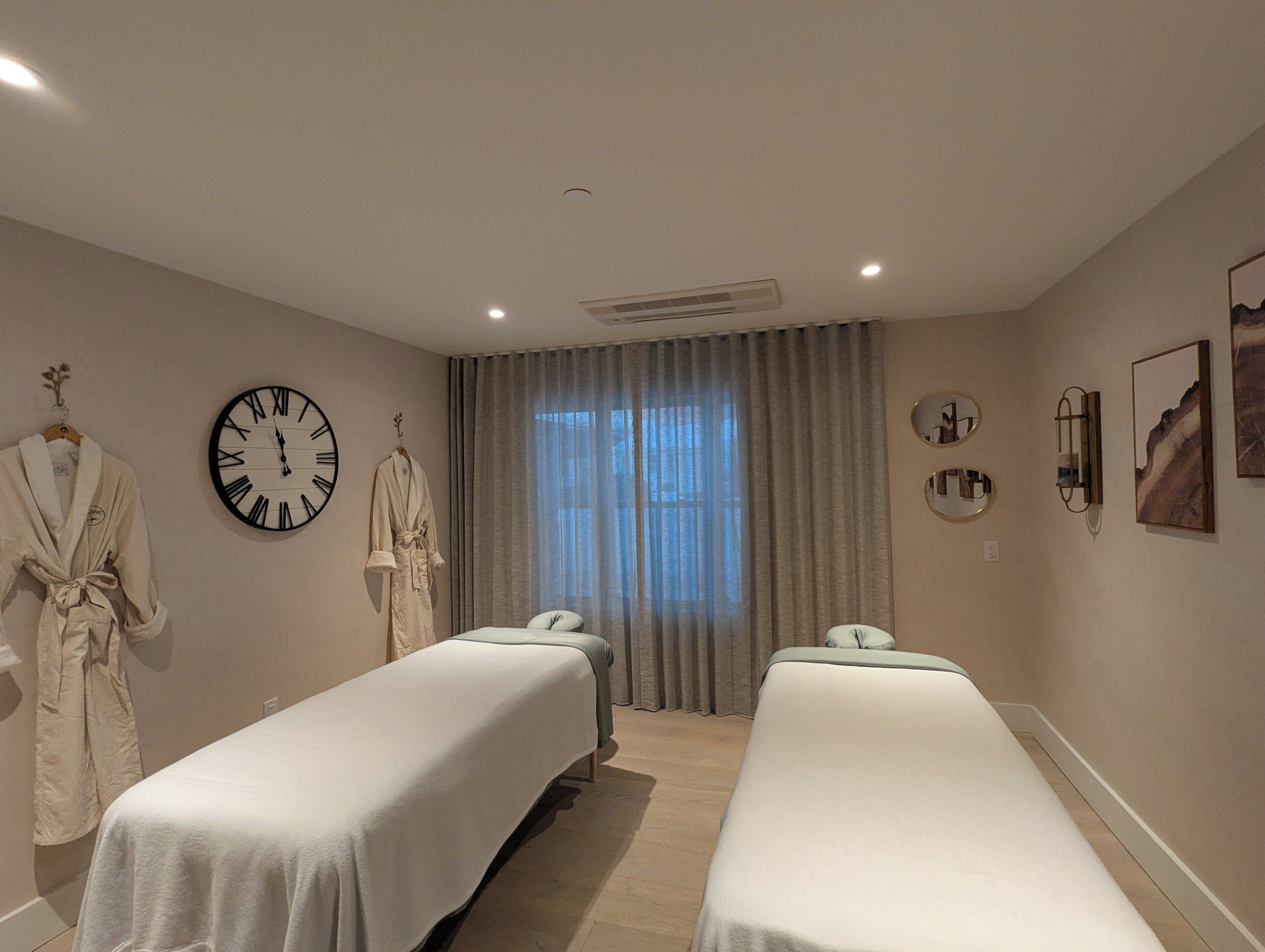 A room with two beds, a clock, and a large window with curtains.