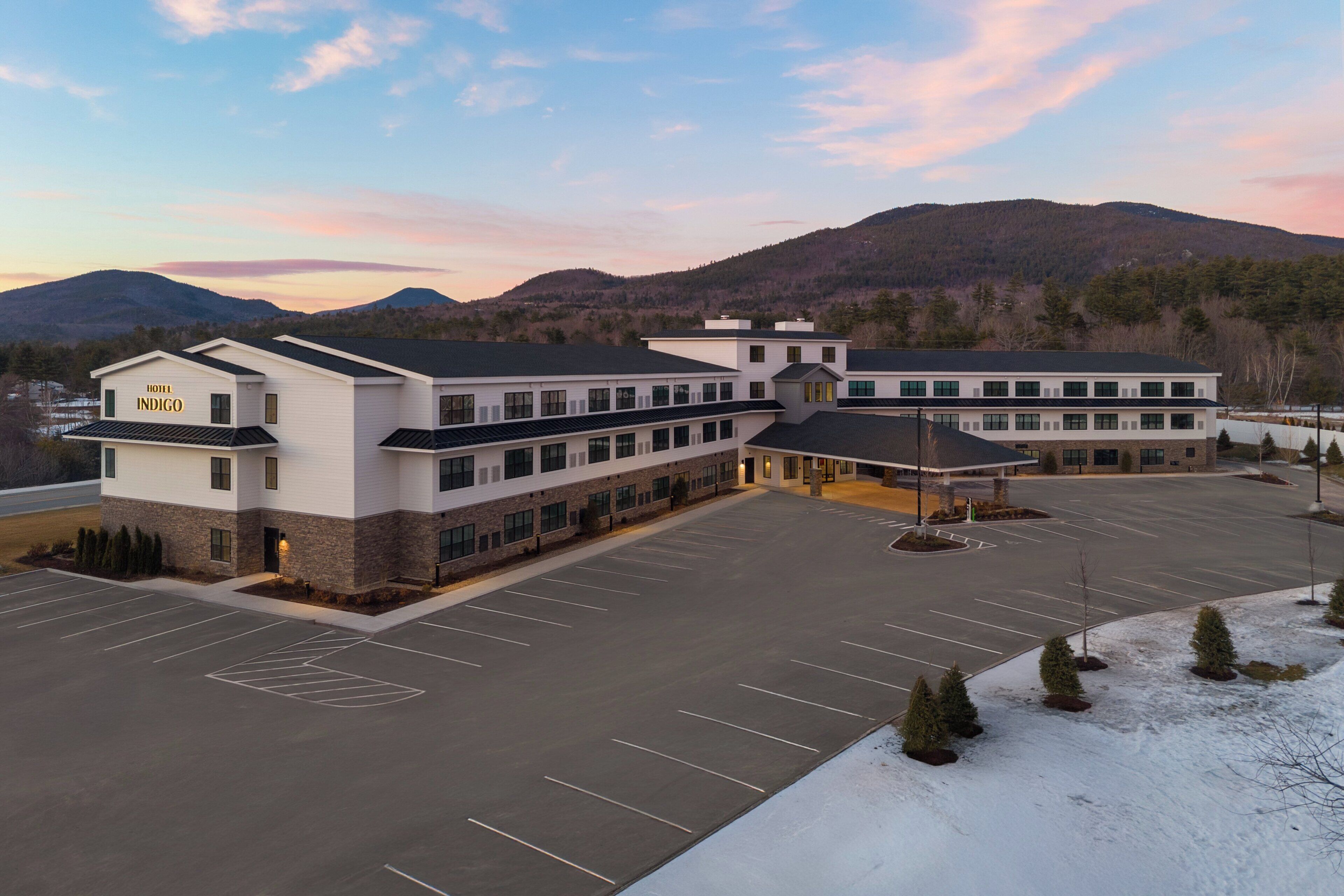 A multi-story hotel with a parking lot and a mountainous backdrop.