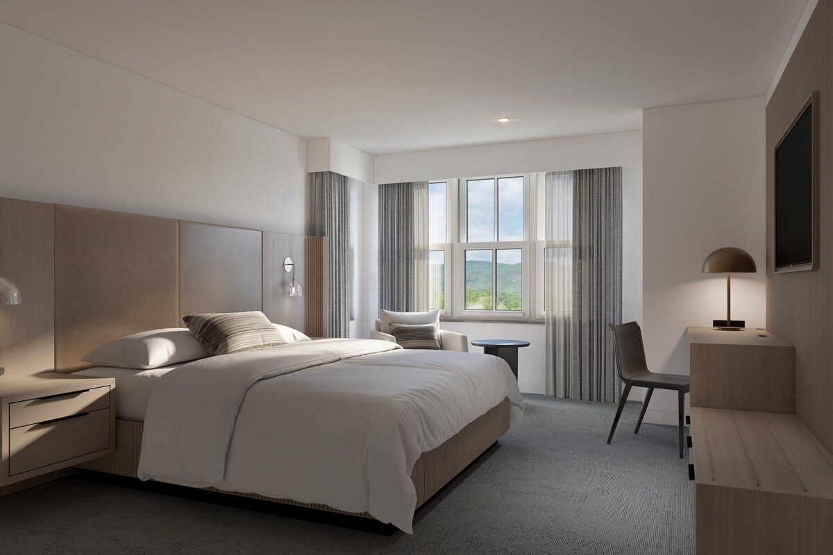 Una habitación de hotel moderna con una cama grande, mesitas de noche, un escritorio, una silla y un televisor.