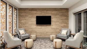 Ein modernes Wohnzimmer mit einer Holzwand, einem Flachbildfernseher, grauen Sesseln, Hocker und einem gemusterten Teppich.