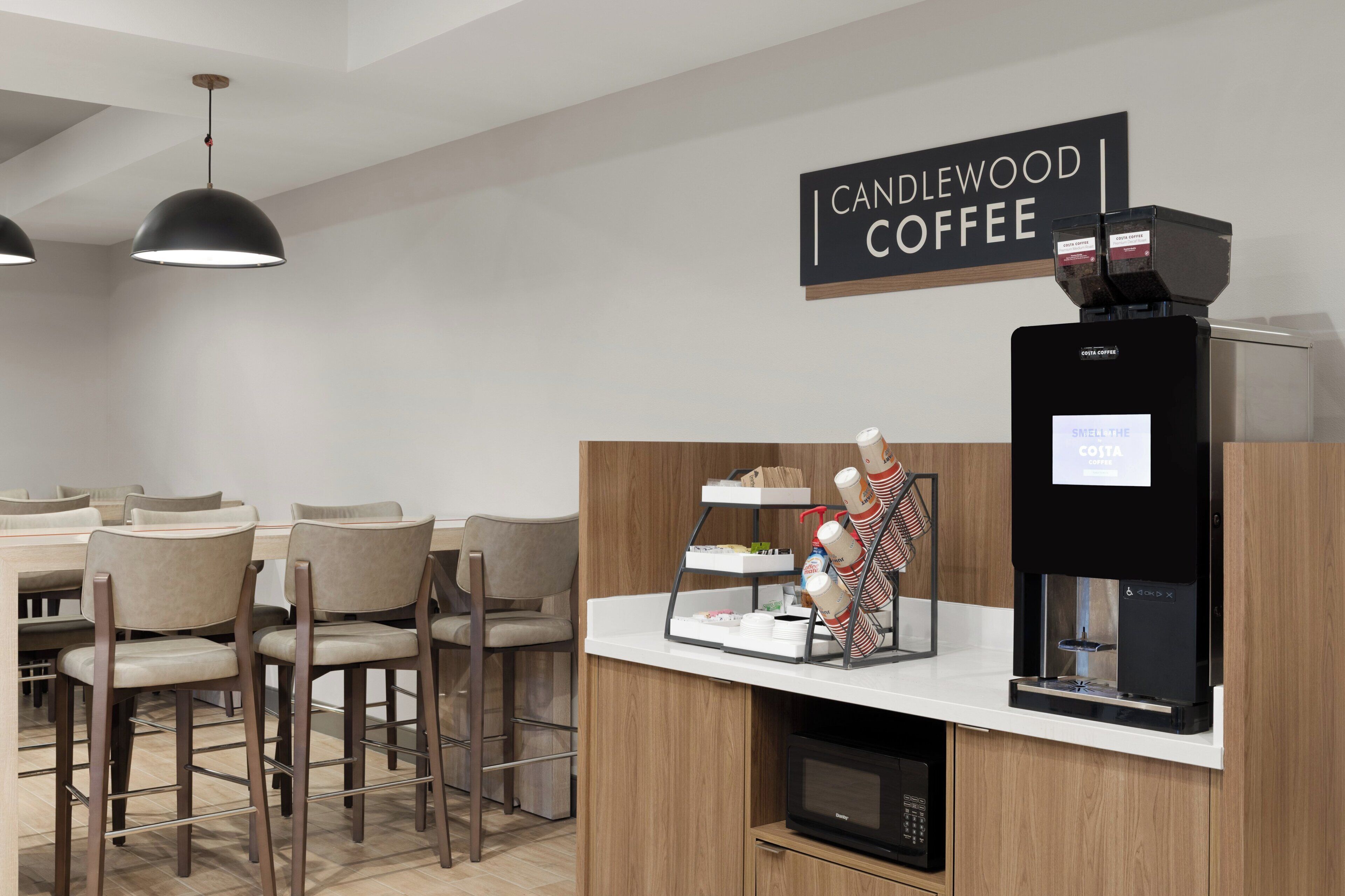 A coffee station with a sign reading 'CANDLEWOOD COFFEE,' a coffee machine, and a display of coffee cups.