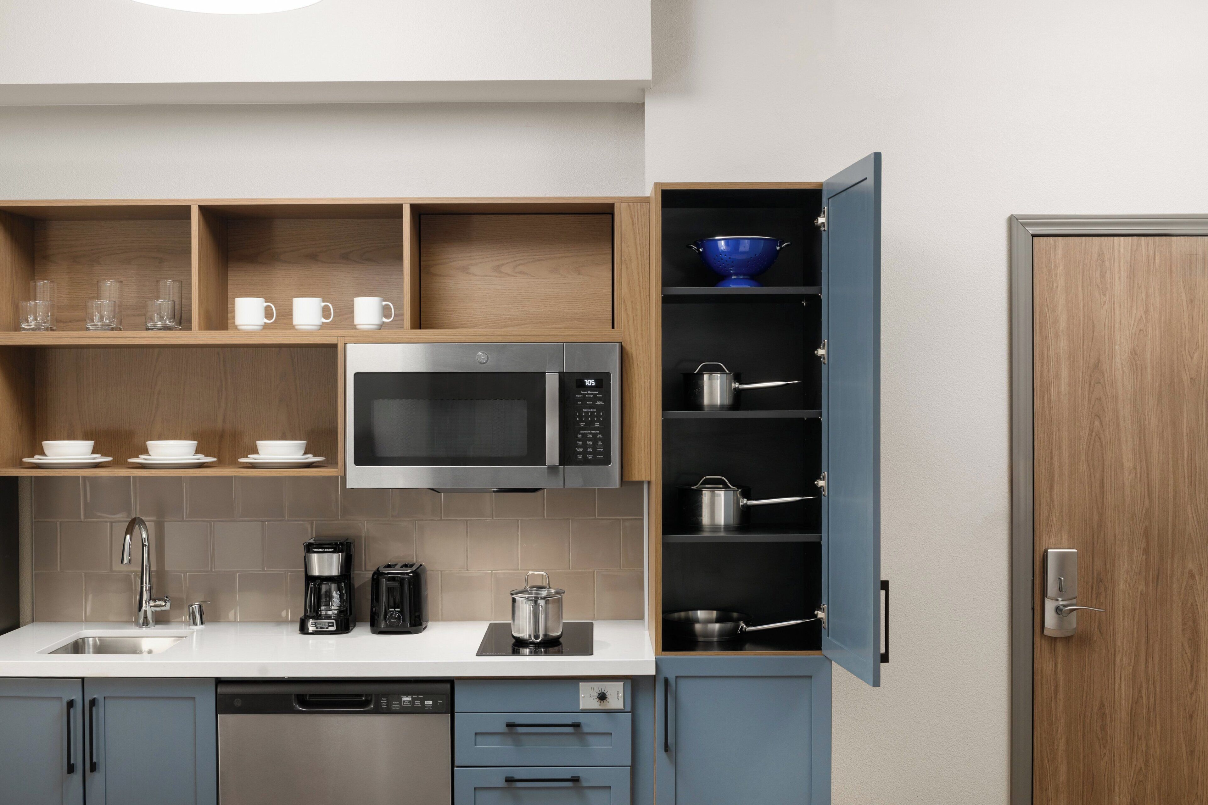 Une cuisine moderne équipée d’un four à micro-ondes, d’une machine à café et de placards ouverts où l’on peut voir les ustensiles de cuisine.
