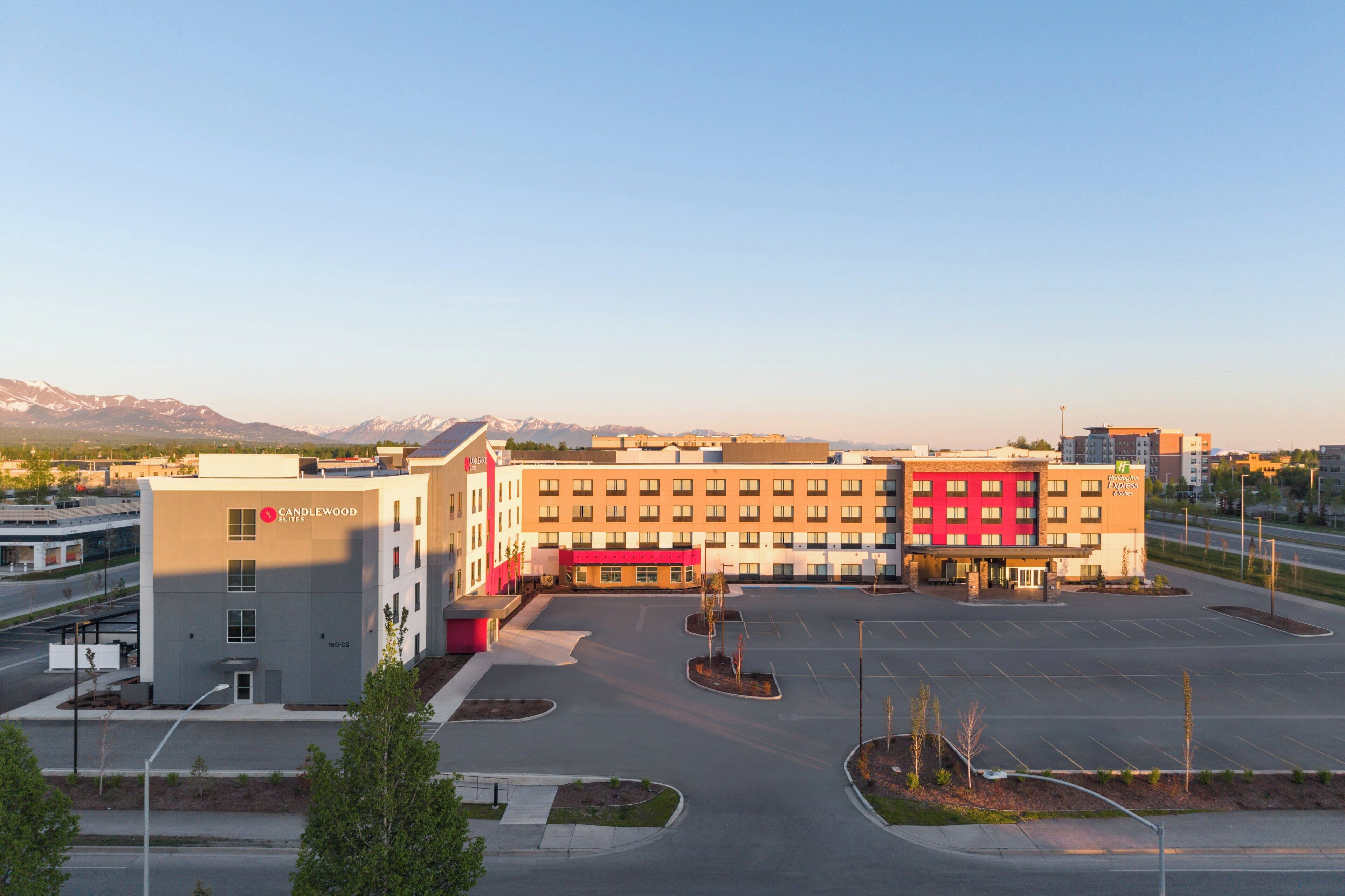 A hotel with a modern design, featuring a parking lot and a view of mountains in the background.
