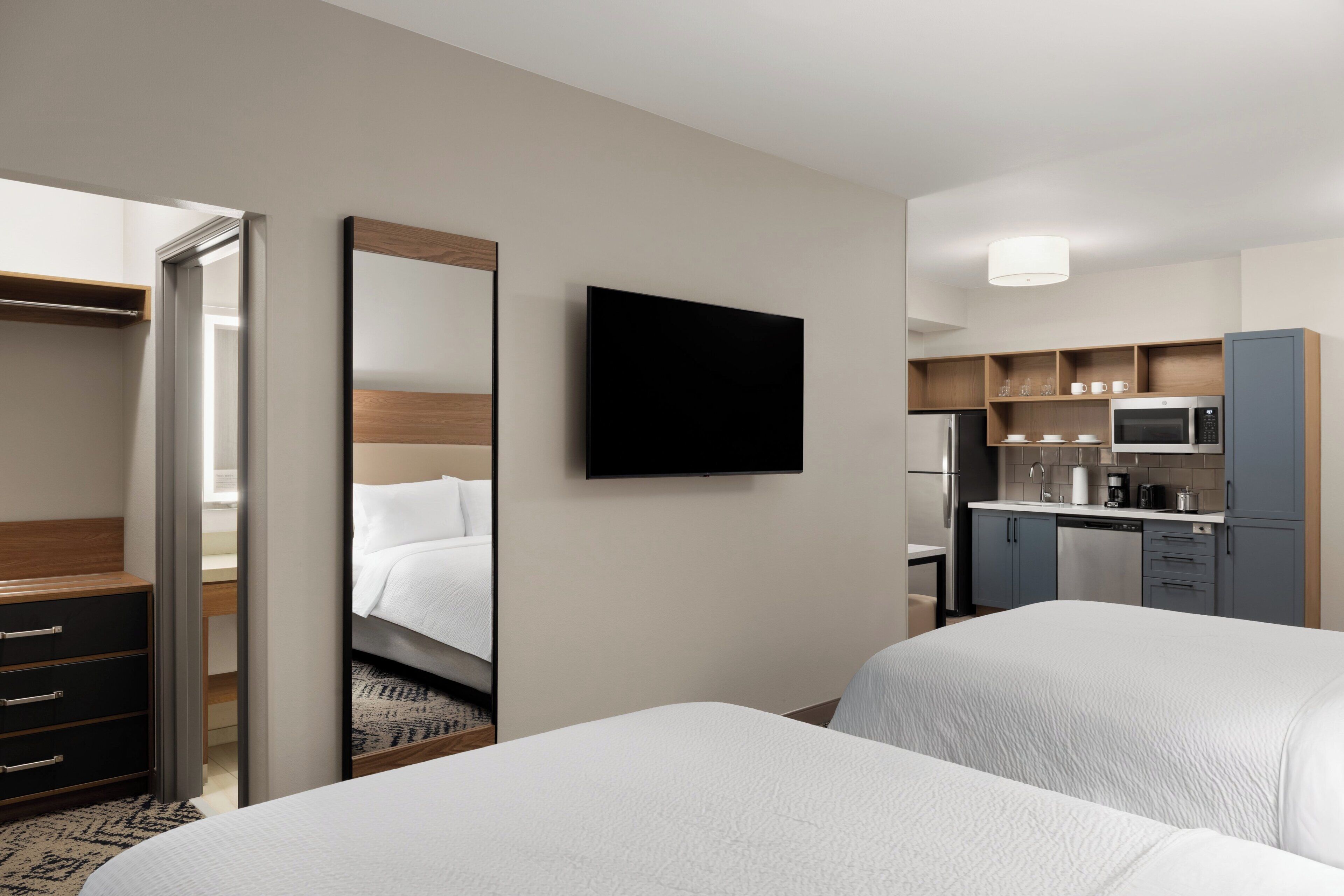 Quarto de hotel com duas camas, televisão, cozinha compacta e closet espaçoso.