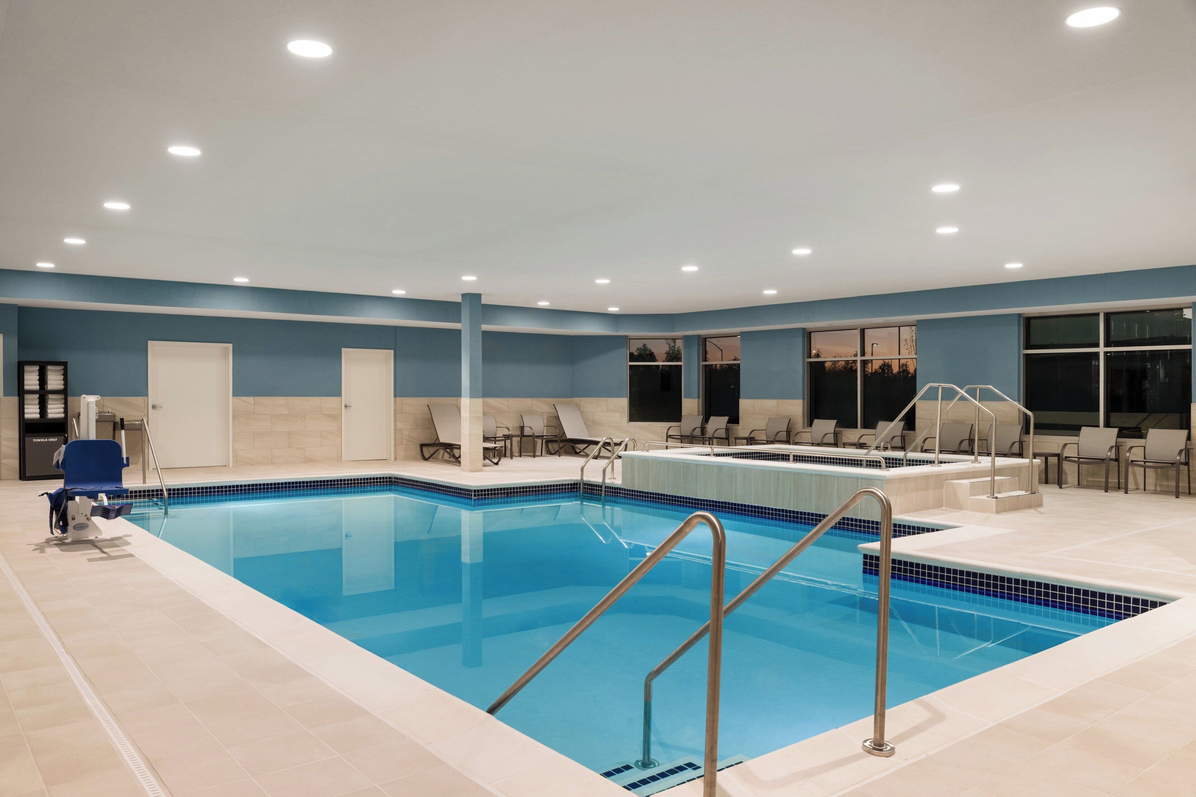 A swimming pool with a tiled deck, lounge chairs, and a changing room with a towel rack.