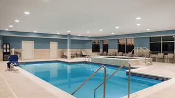 A swimming pool with a tiled deck, lounge chairs, and a changing room with a towel rack.