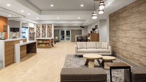 Een moderne receptiezone met een houten receptiebalie, een zithoek met een bank en ronde tafels, en een wand met geometrische patronen.