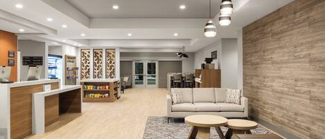 A modern reception area with a wooden reception desk, seating area with a sofa and round tables, and a wall with geometric patterns.