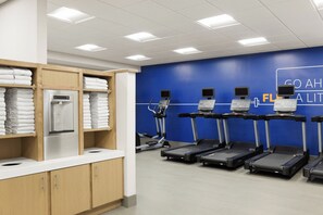 Un gimnasio con cintas de correr, una fuente de agua y toallas ordenadas.