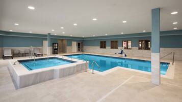A large indoor swimming pool with a jacuzzi, tiled walls, and a ceiling with recessed lighting.