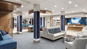A modern hotel lobby with seating areas, a reception desk, and a visible kitchen area. - Holiday Inn Express And Suites Anchorage Midtown by IHG (Anchorage)