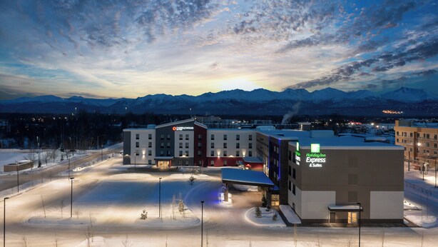 A Holiday Inn Express building with a snow-covered parking lot and mountains in the background. - Holiday Inn Express And Suites Anchorage Midtown by IHG (Anchorage)