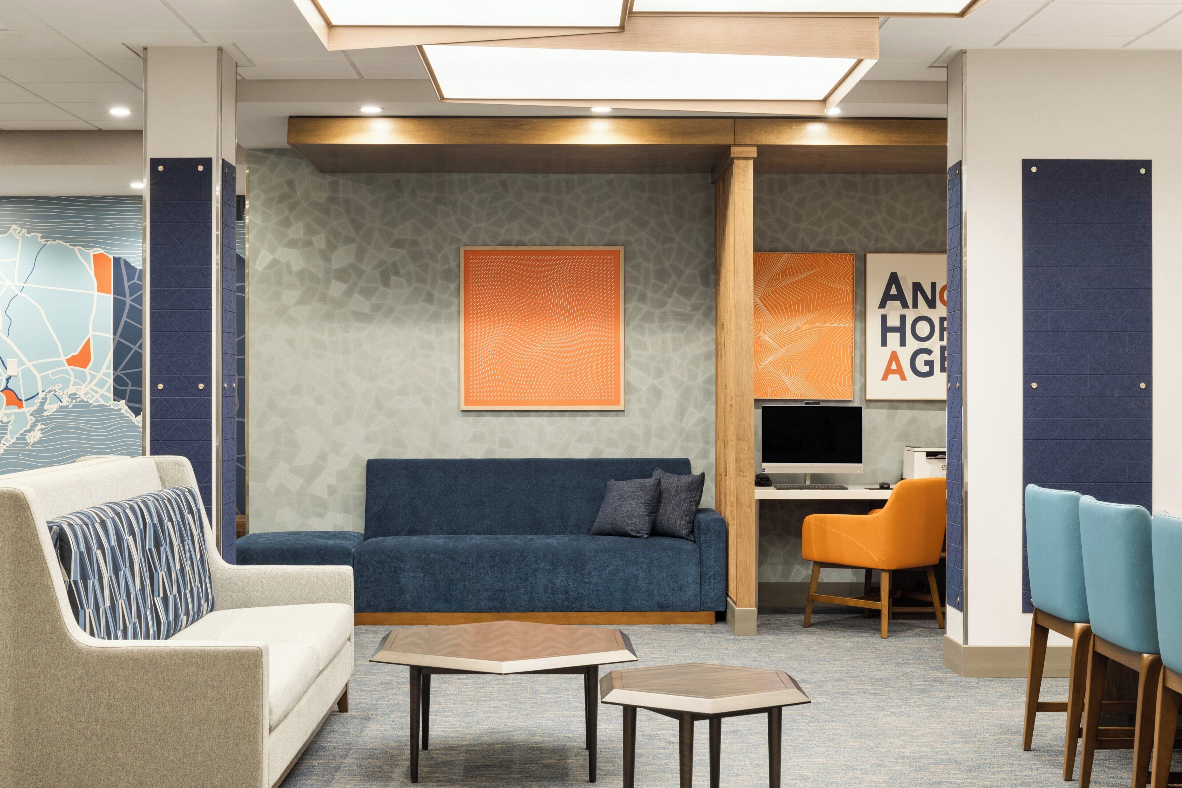 A modern lounge area with a sofa, chairs, a small table, and a desk with a computer.